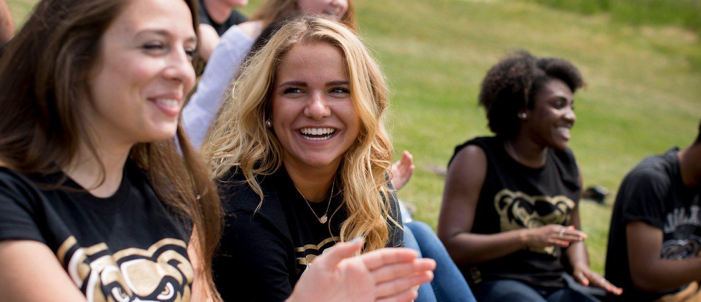 Female student, sitting outside, laughs with a group of friends